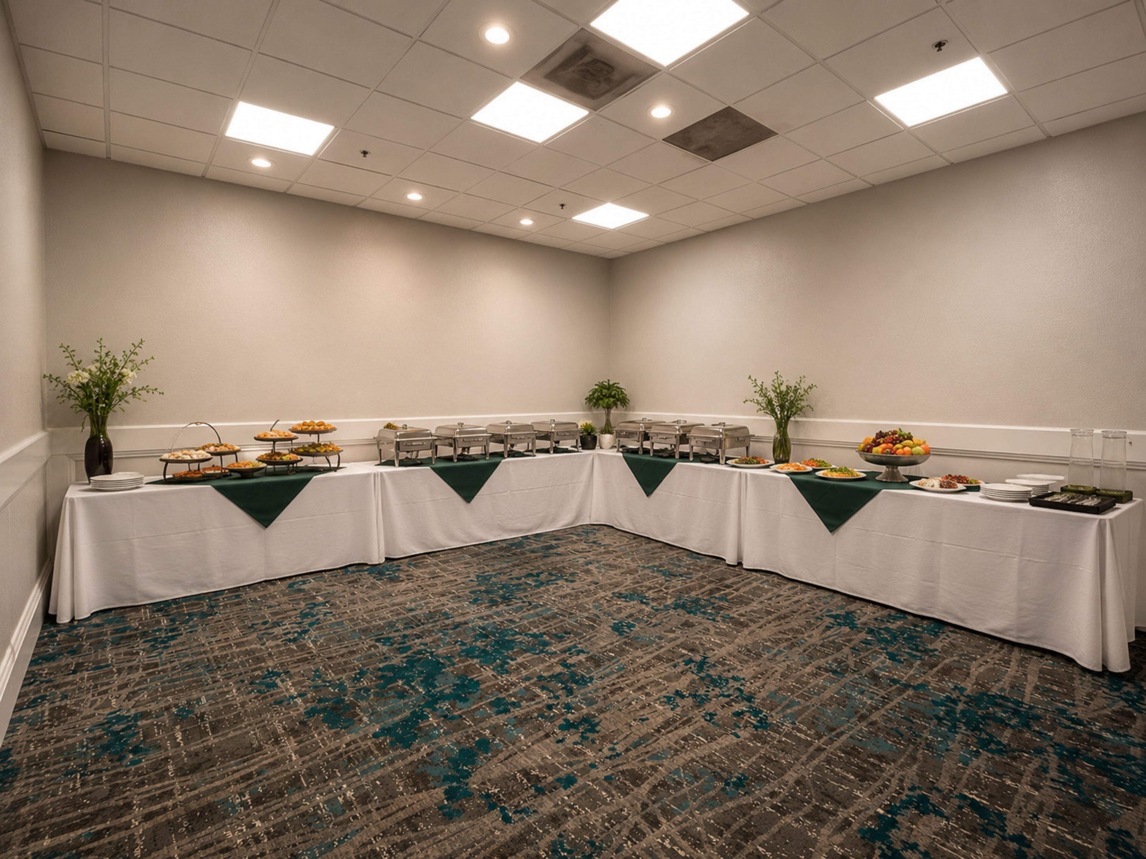 Un salón de conferencias con una larga mesa, varias estaciones de comida y una alfombra estampada.
