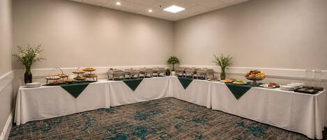 Un salón de conferencias con una larga mesa, varias estaciones de comida y una alfombra estampada.