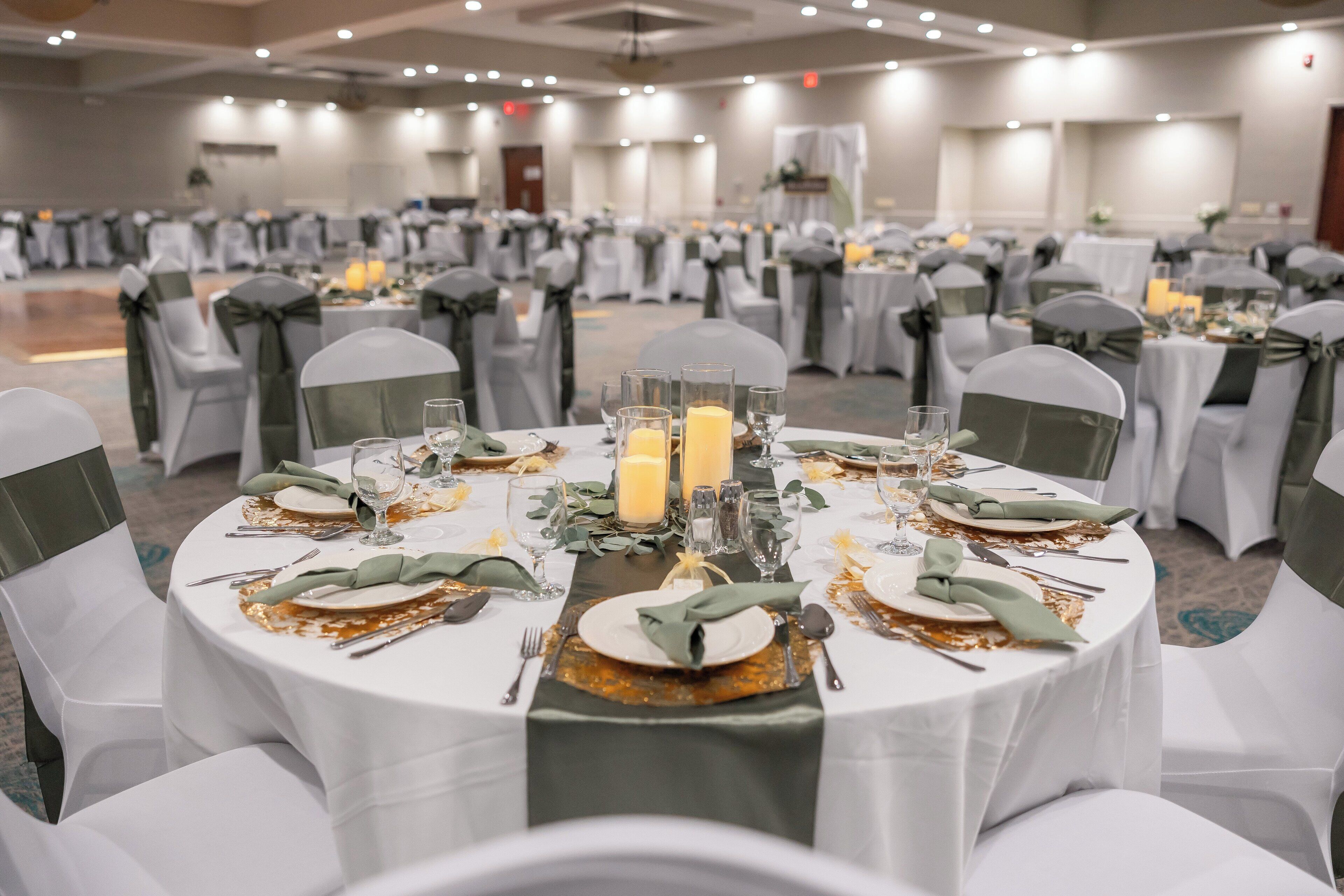 A banquet hall with round tables set for a formal event, featuring white tablecloths, green napkins, and candle centerpieces.