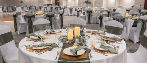 A banquet hall with round tables set for a formal event, featuring white tablecloths, green napkins, and candle centerpieces.