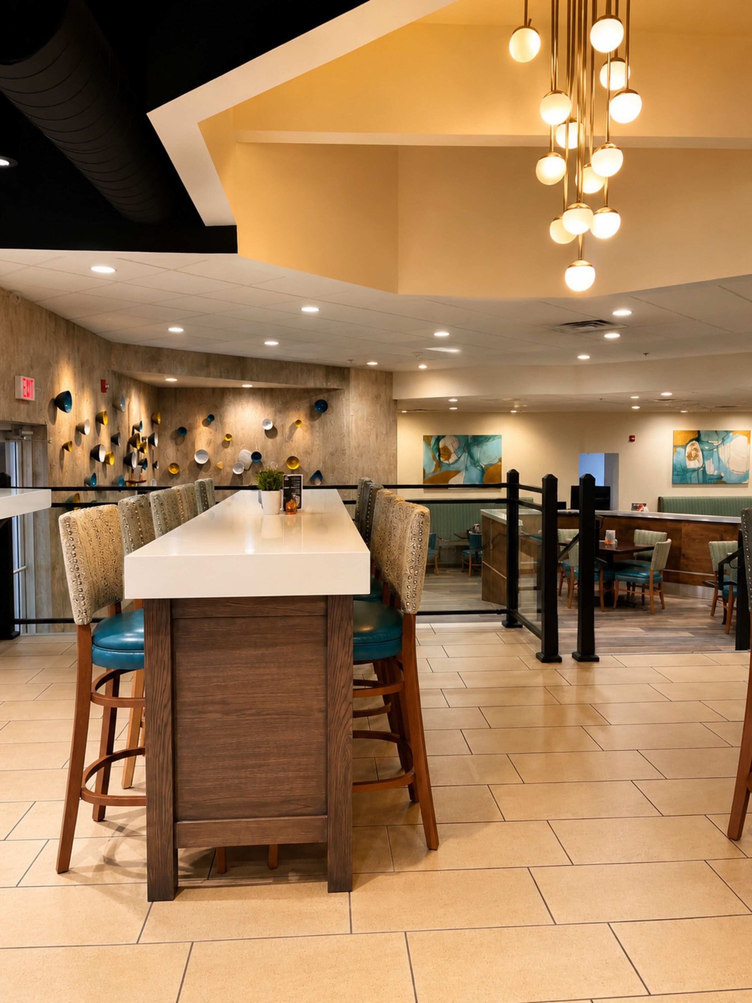 A modern restaurant interior with a long rectangular table, wooden chairs, and a hanging light fixture.