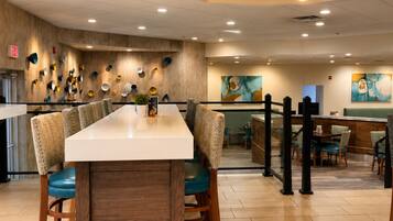A modern restaurant interior with a long rectangular table, wooden chairs, and a hanging light fixture.