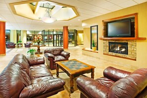 A lobby with leather sofas, a fireplace, a television, and a large window overlooking the lobby area.