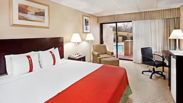 A hotel room with a large bed, a desk, a chair, and a view of the outdoors.