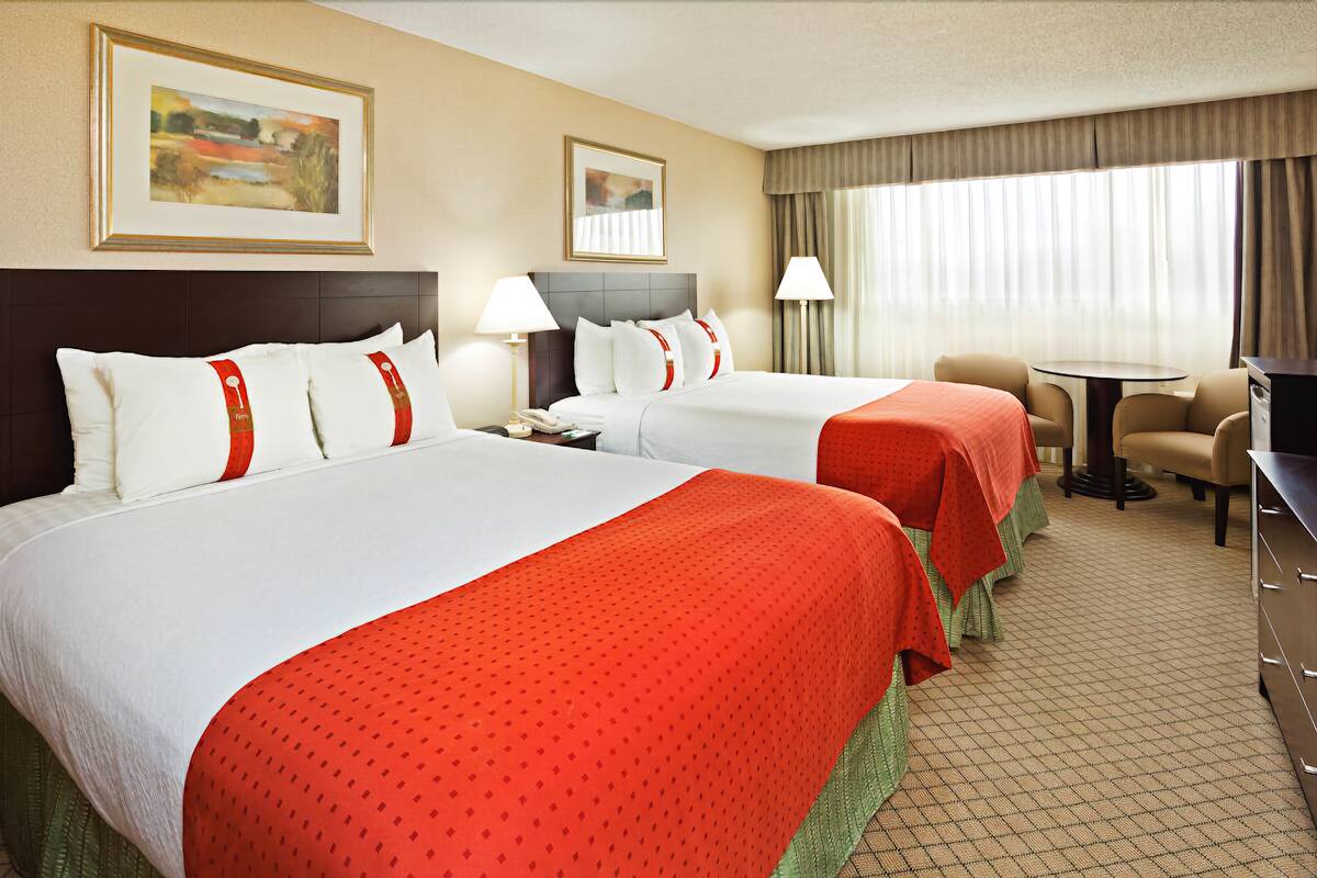 A hotel room with two beds, a desk, a chair, a TV, and a window with curtains.