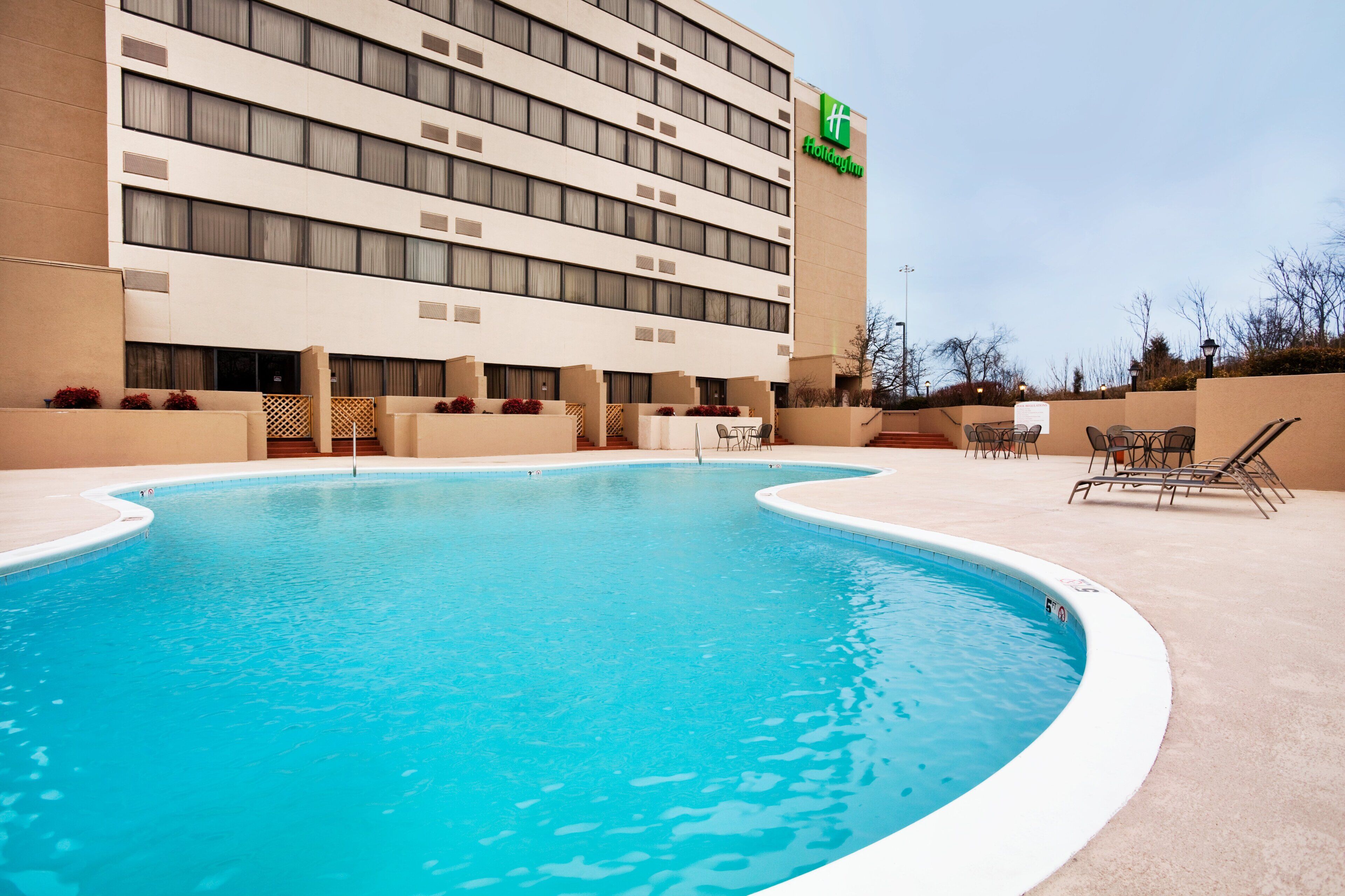 A hotel with a swimming pool, outdoor seating, and a clear sky.