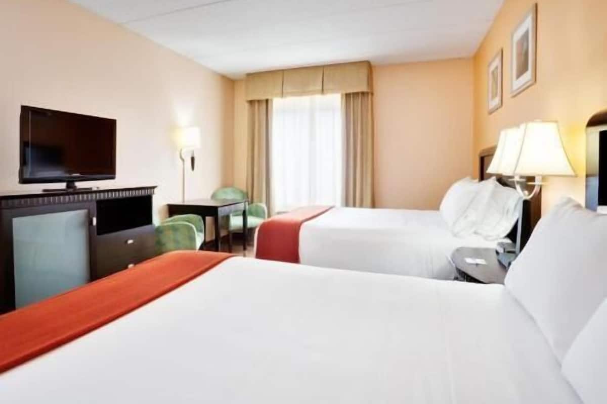 A hotel room with two beds, a TV, a desk, and a chair.