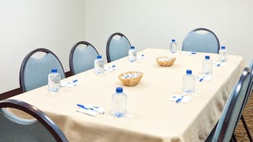 Un salón de conferencias con una larga mesa, sillas, botellas de agua y un cesto.