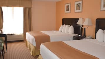 Une chambre d’hôtel avec deux lits, un bureau, une chaise, une lampe et un téléphone sur une table de chevet.
