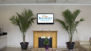 Zona de recepción de un Baymont Inn & Suites, con una televisión, dos plantas en macetas, una chimenea y un sofá de cuero.