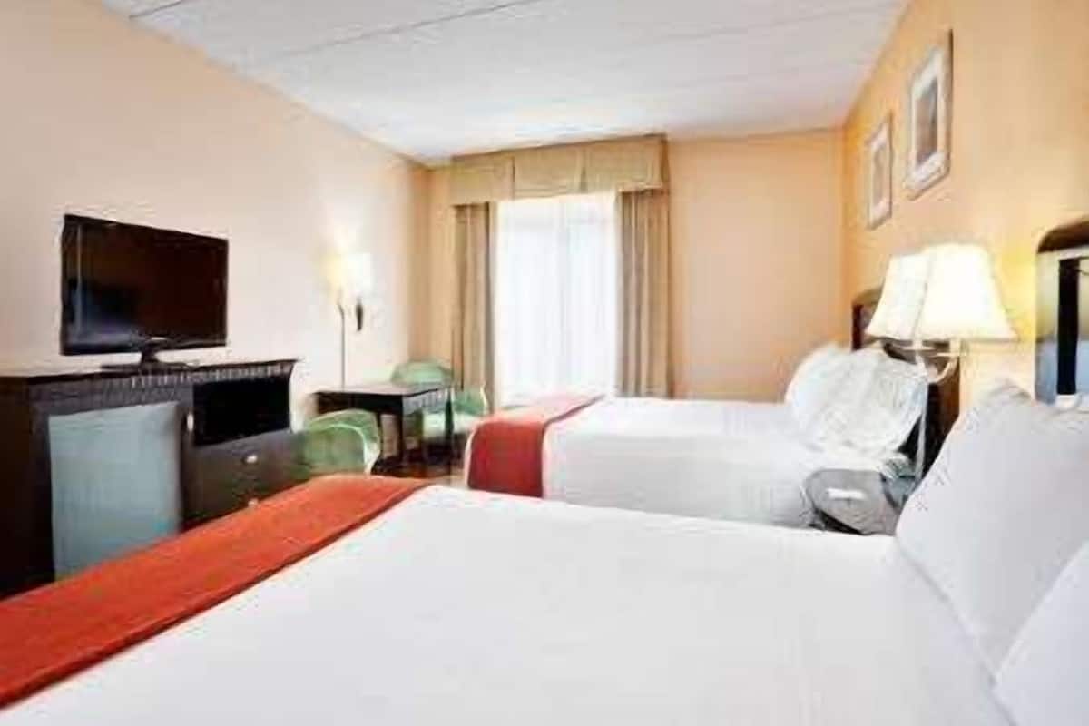 A hotel room with two beds, a TV, a desk, and a window with curtains.