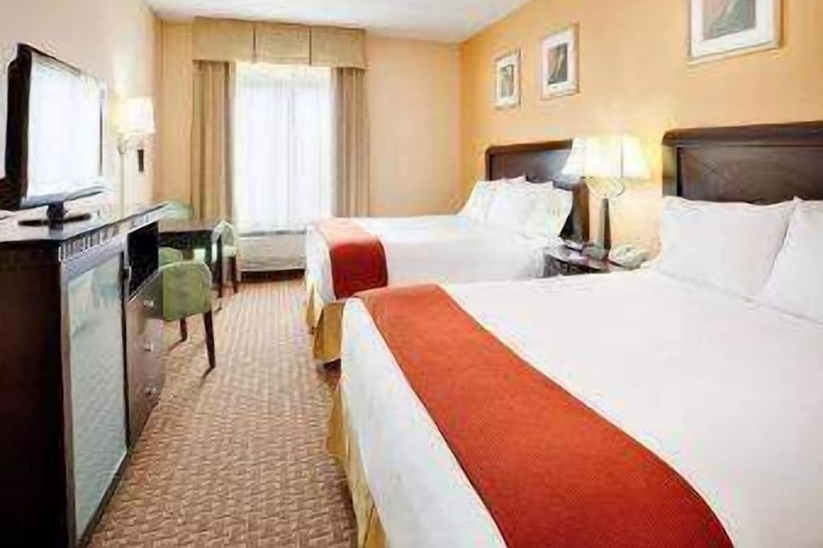 A hotel room with two beds, a desk, a chair, and a television.