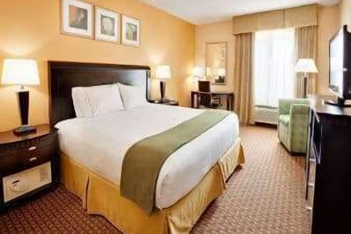 A hotel room with a large bed, bedside tables, a desk, a chair, and a television.