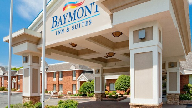 Un Baymont Inn & Suites con un letrero llamativo, edificios de ladrillo y un área de entrada ajardinada.