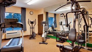 Un gimnasio con varios equipos de ejercicio, un reloj en la pared y amplias ventanas.