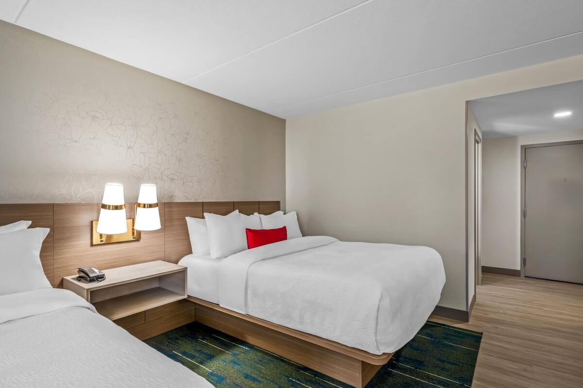 Una habitación de hotel con cama, mesitas de noche, lámparas y una puerta.