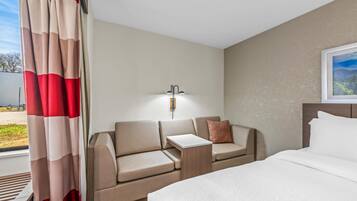 A hotel room with a bed, a sofa, a nightstand, and a window with curtains.