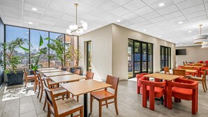 A modern dining area with wooden tables and chairs, large windows, and indoor plants. - Sonesta Select Hotels Statesville (Statesville)