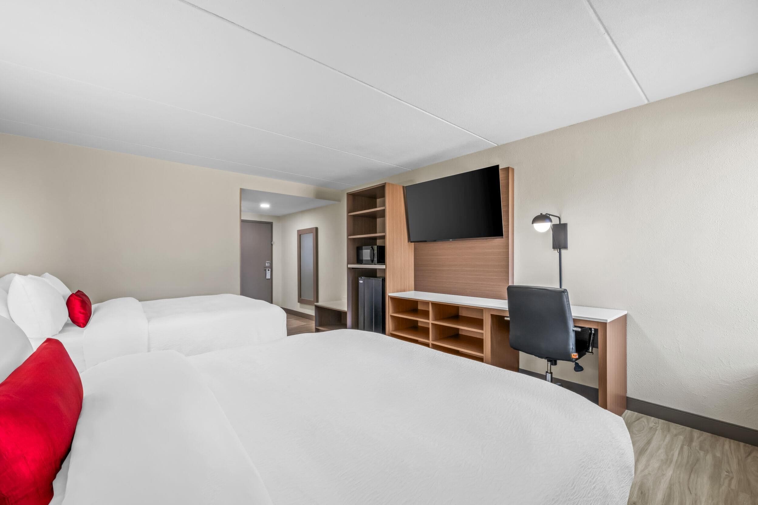 Habitación de hotel con dos camas, televisión, escritorio con silla y una kitchenette pequeña.