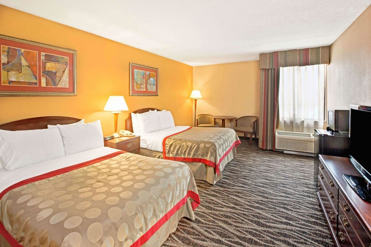 A hotel room with two beds, a television, a desk, and a chair.