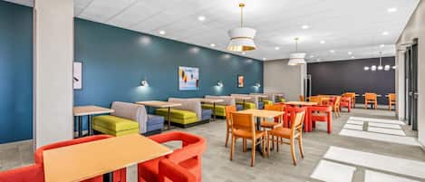 A modern indoor seating area with tables and chairs, a blue wall with artwork, and a ceiling with recessed lighting.