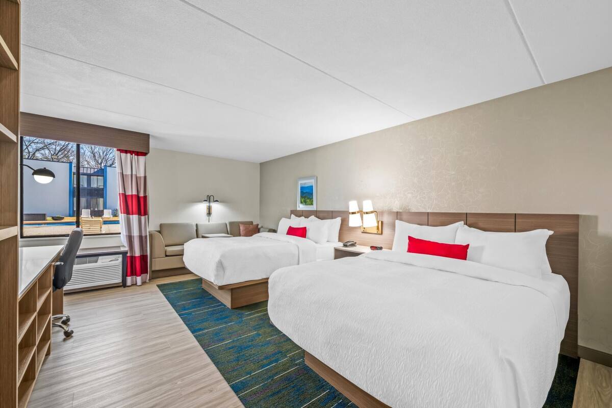 Habitación de hotel con dos camas, un escritorio y vistas al exterior.