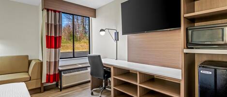 A modern hotel room with a bed, a desk, a chair, a television, and a built-in microwave.