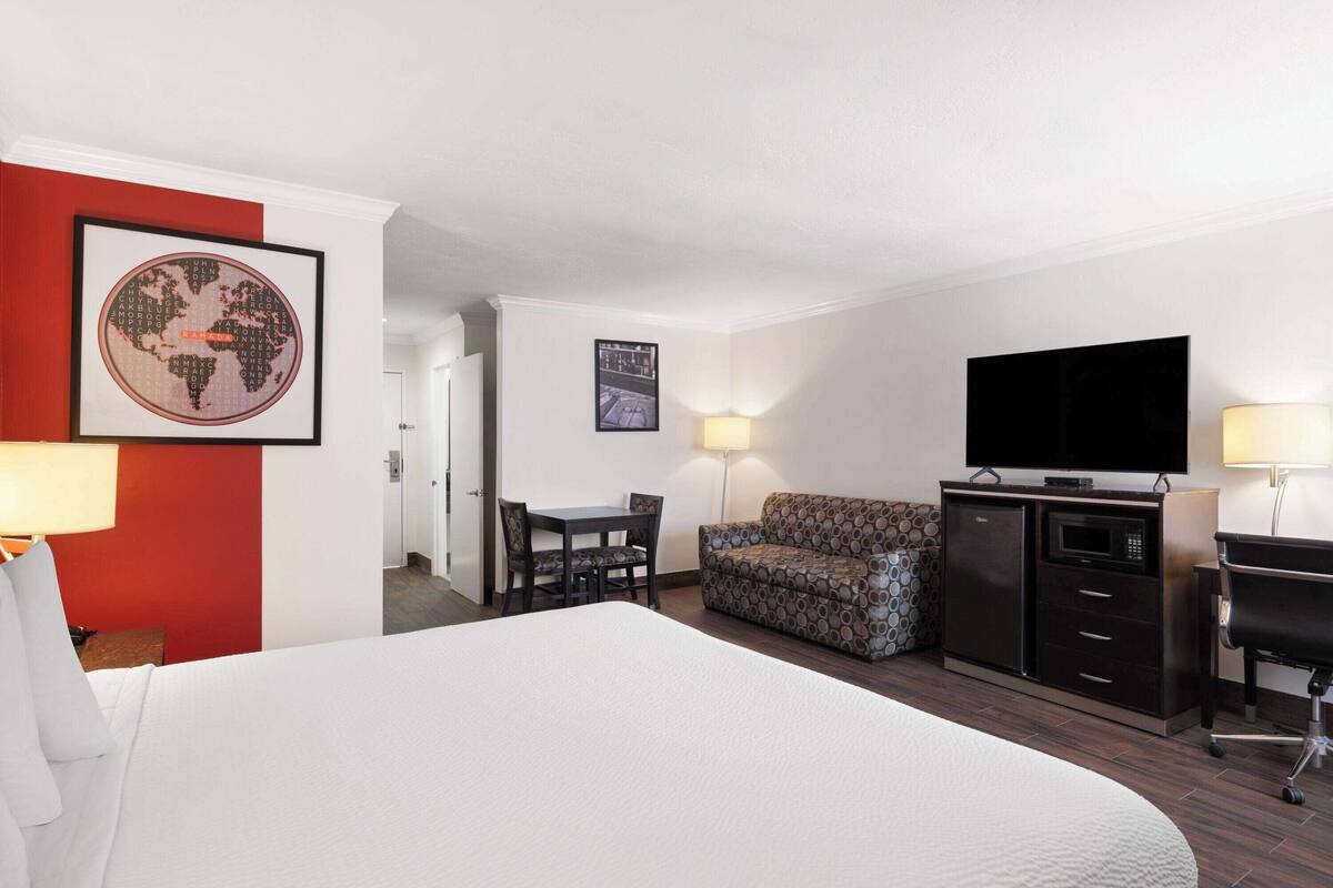 Quarto de hotel com uma cama grande, sofá, televisão, escrivaninha e micro-ondas.
