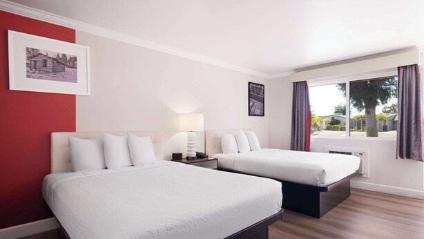 Habitación de hotel con dos camas, una ventana con cortinas e imagen colgada en la pared.