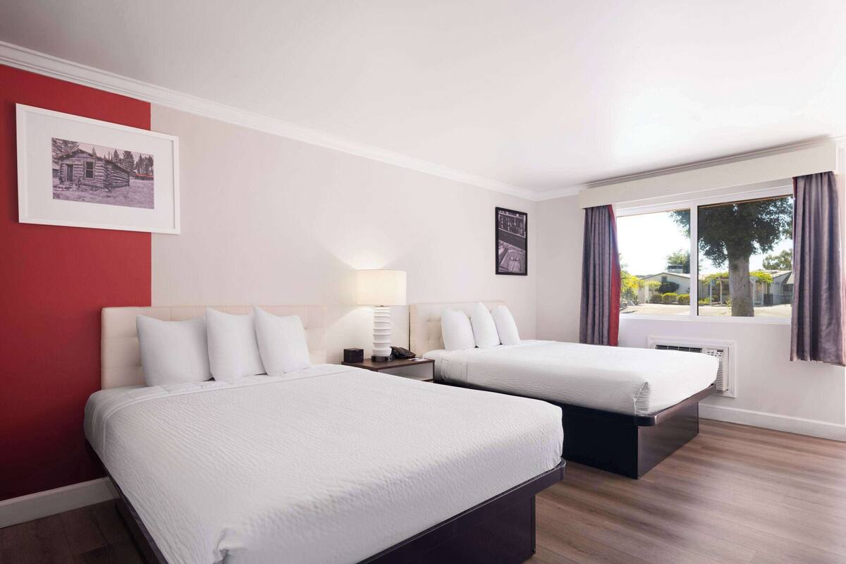 Quarto de hotel com duas camas, uma janela com cortinas e um quadro na parede.
