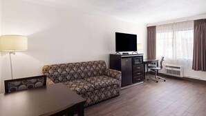 Una habitación de hotel con sofá, televisión, escritorio y silla.