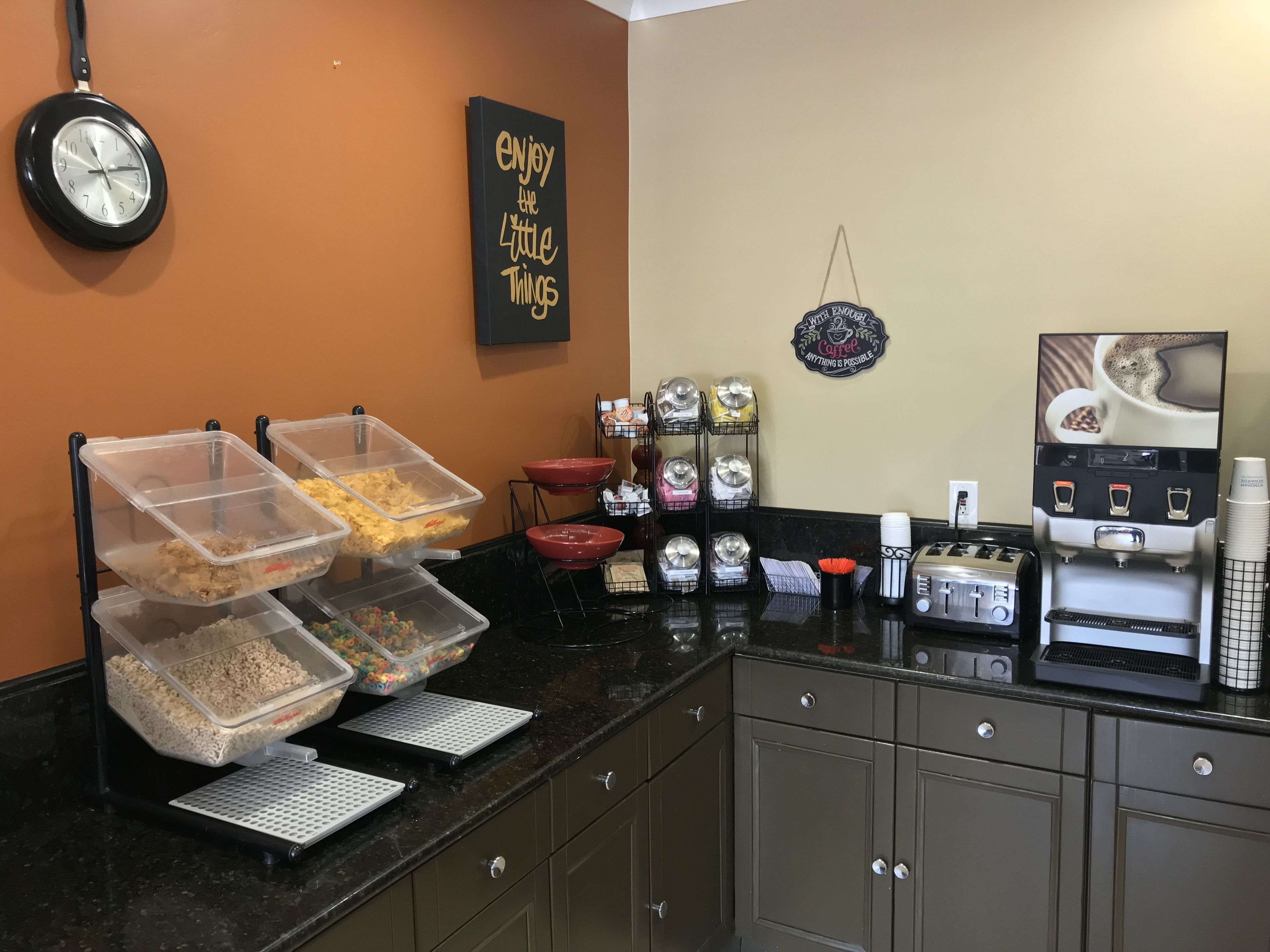 A kitchen area with a coffee station, a clock, and a motivational sign.