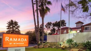 Señal de Ramada by Wyndham, un edificio de fachada de ladrillo, palmeras y una bandera.