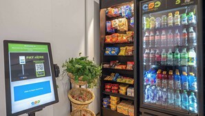 Un área de autoservicio con una terminal de pago digital, una máquina expendedora de aperitivos y un dispensador de bebidas.