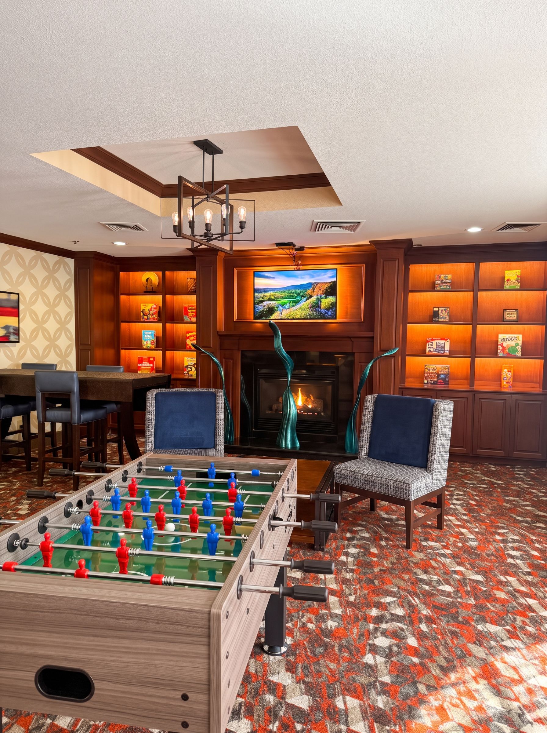 A room with a foosball table, two chairs, a television, and a fireplace.