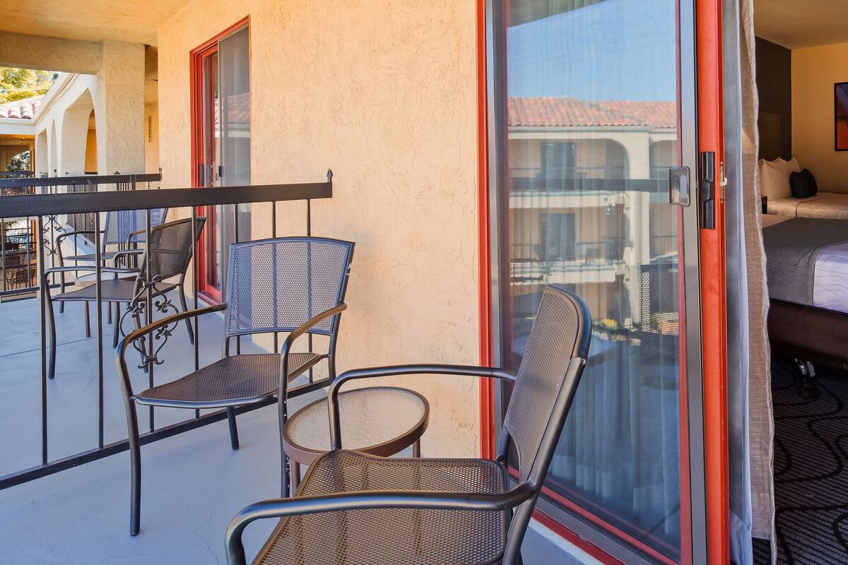 A hotel room with a balcony, a bed, and a dining area with chairs and a table.