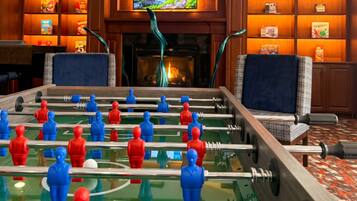 A room with a foosball table, a television mounted above a fireplace, and bookshelves.