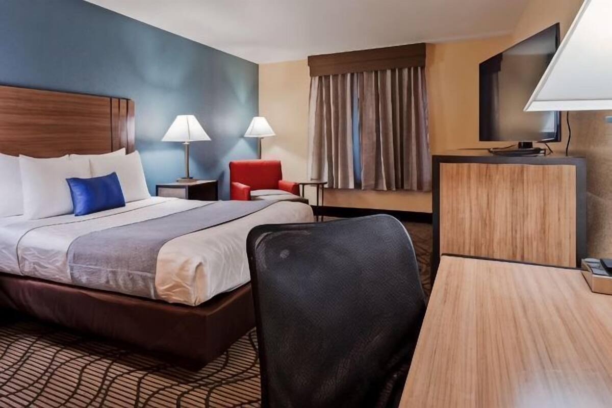 A hotel room with a bed, two bedside lamps, a desk, a chair, a TV, and a window with curtains.