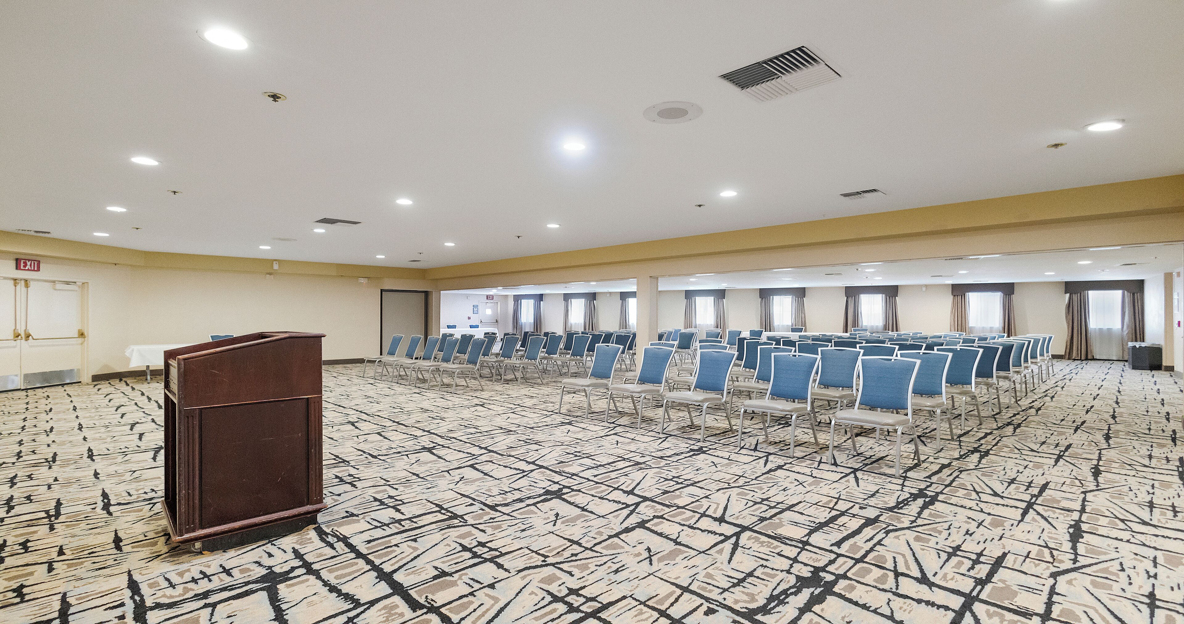 A large conference room with rows of blue chairs, a podium, and a patterned carpet.