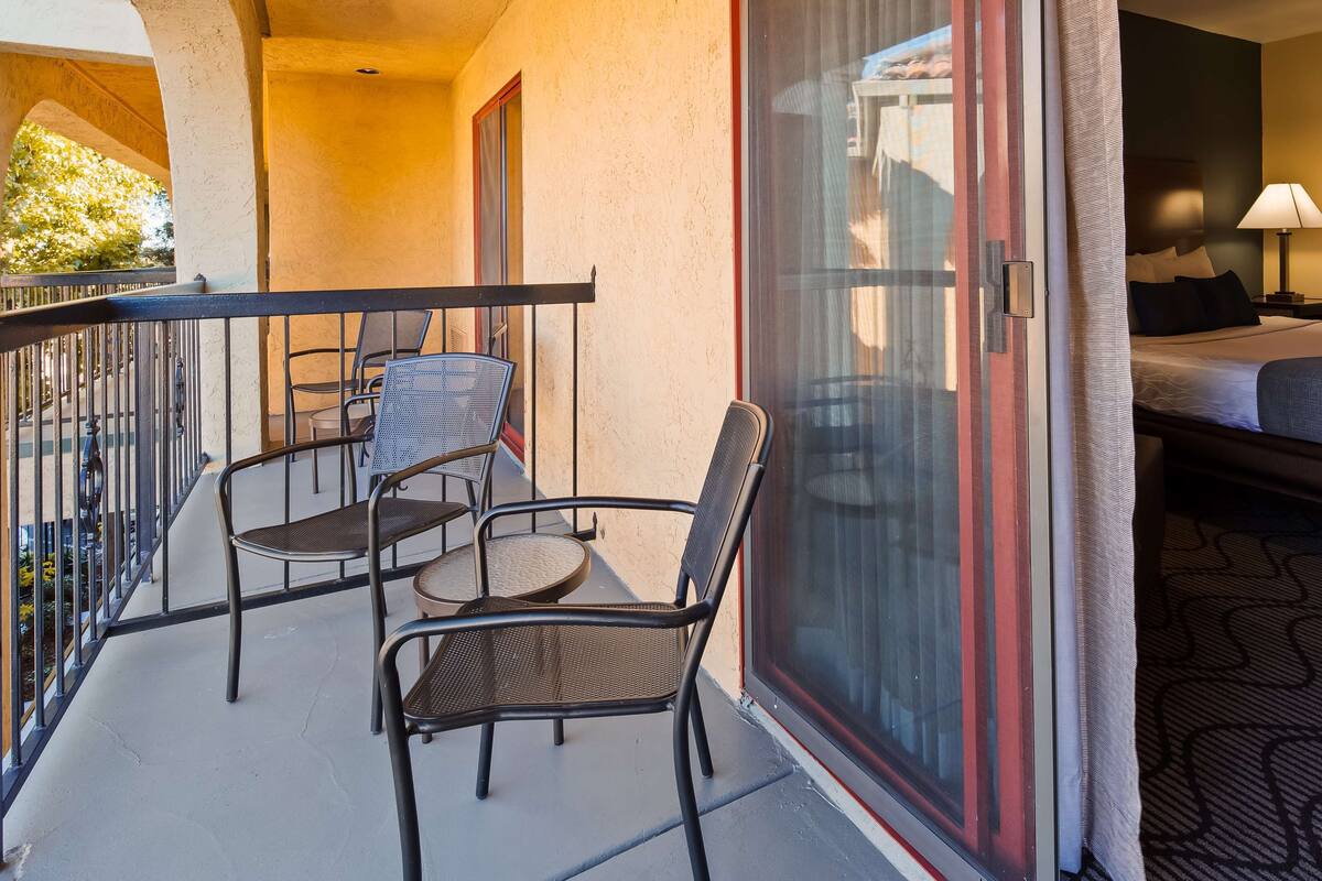 A hotel room with a balcony, a bed, a nightstand, and a lamp.