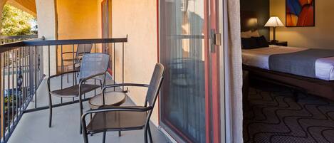 A hotel room with a balcony, a bed, a nightstand, and a lamp.
