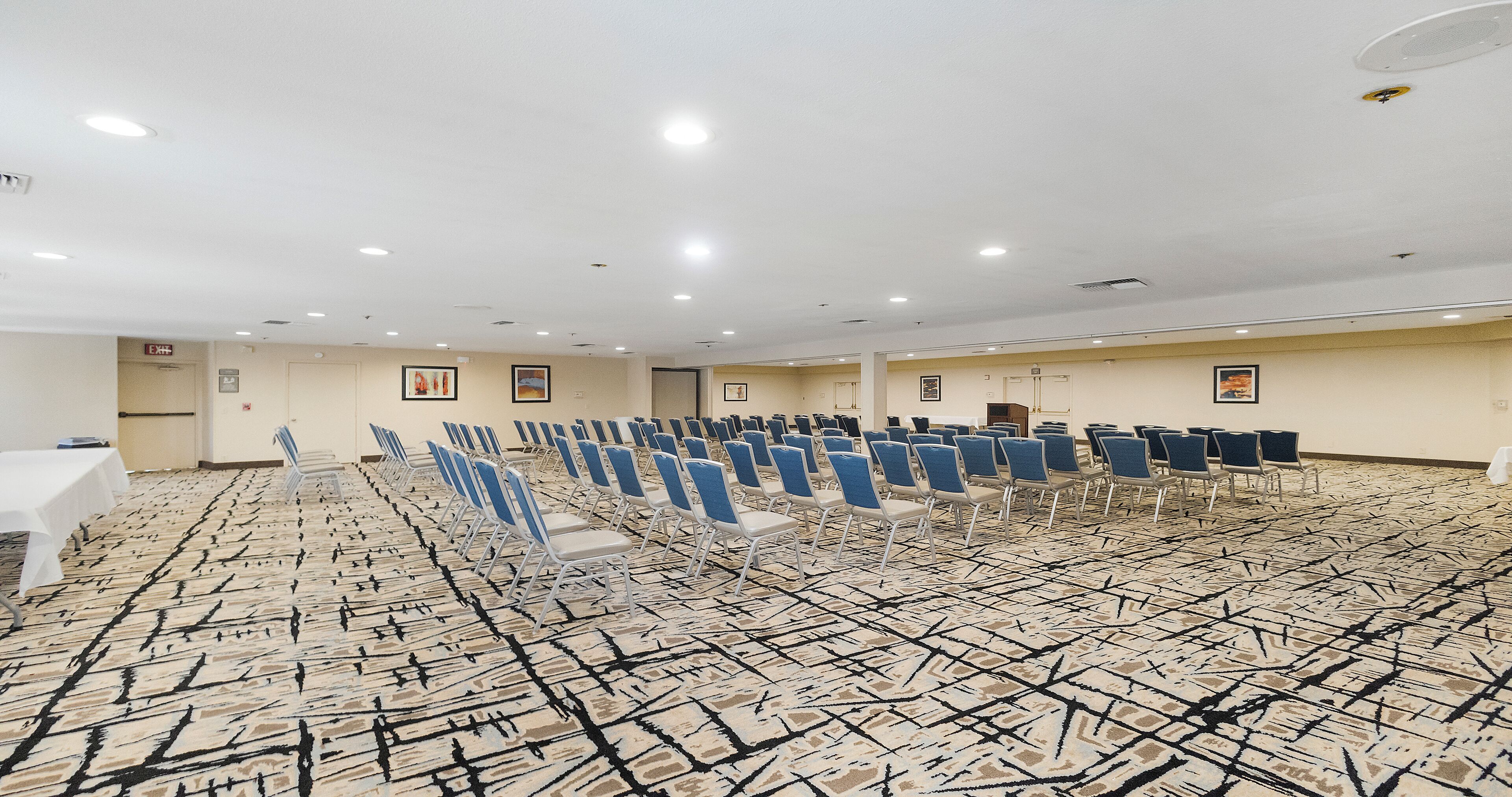 A conference room with rows of chairs, a white table, and a patterned carpet.