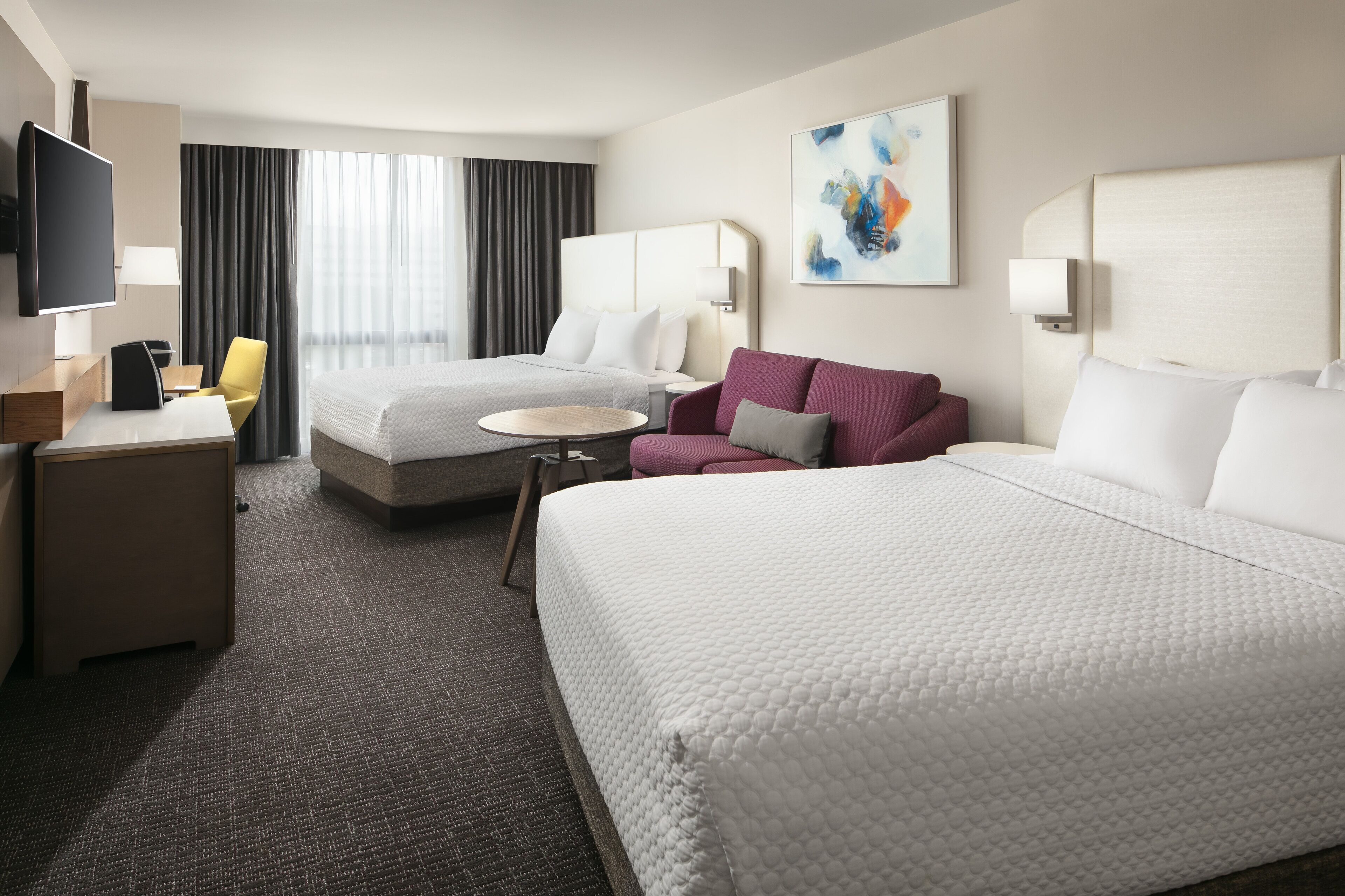 A hotel room with two beds, a desk with a chair, a TV, and a painting on the wall.