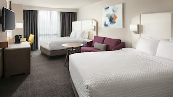 A hotel room with two beds, a desk with a chair, a TV, and a painting on the wall.
