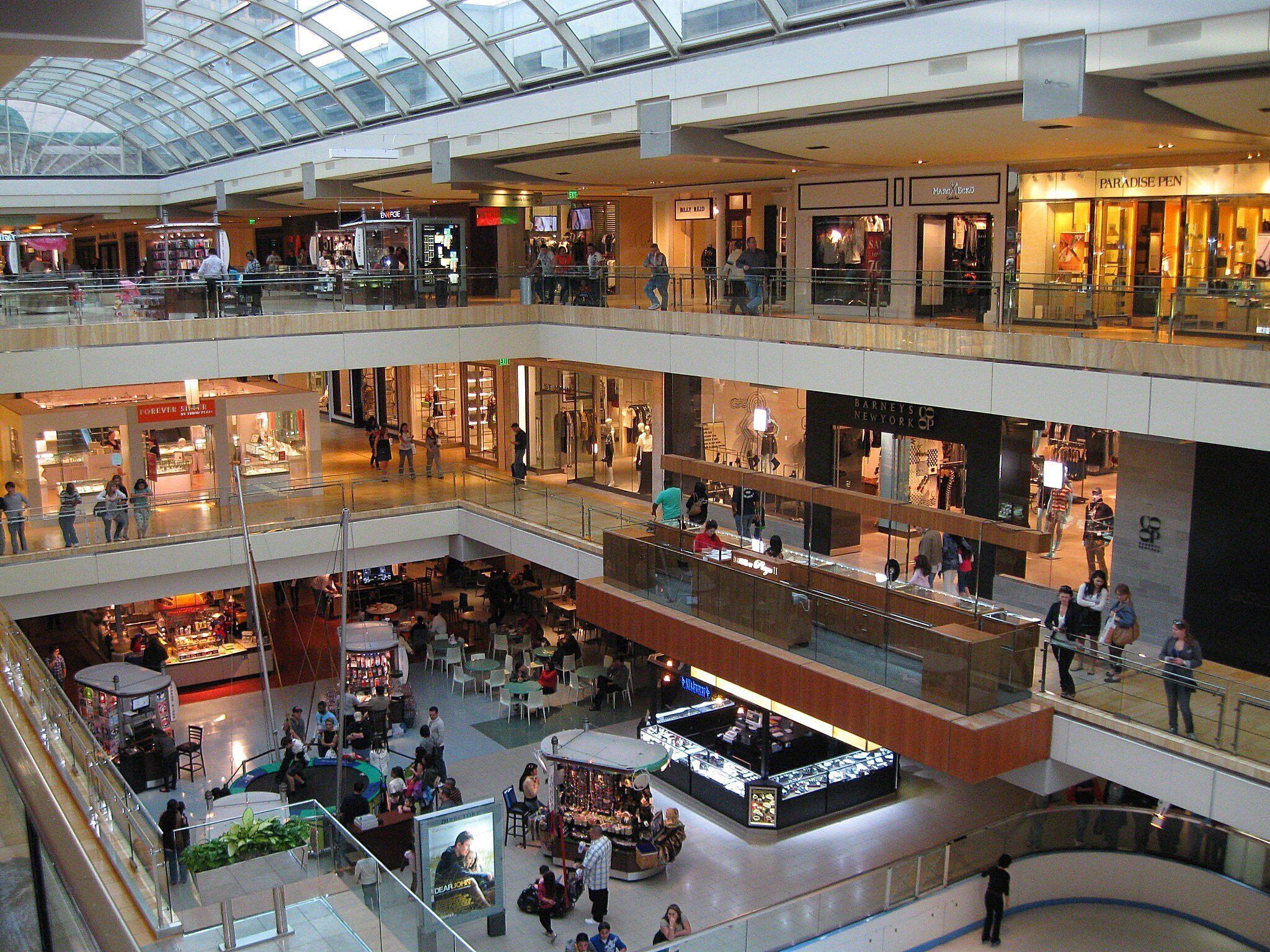 Un centro comercial de varios niveles con diversas tiendas, un patio de comidas y un techo de vidrio.