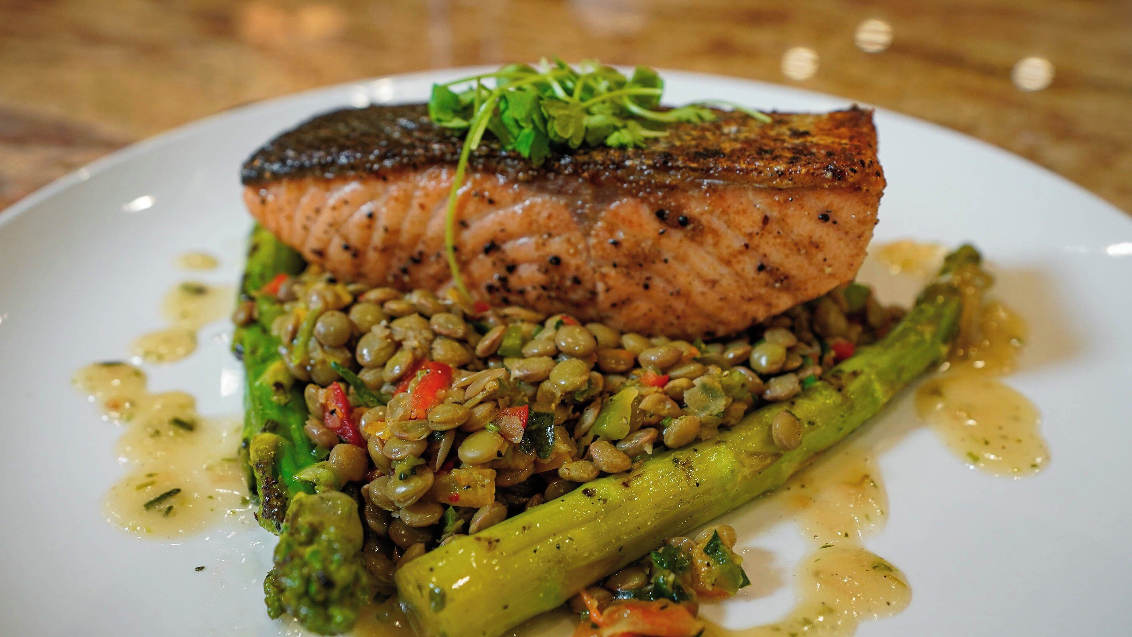 Une assiette contenant un morceau de saumon grillé, des lentilles et des asperges.