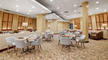 A hotel lobby with multiple seating areas, including round tables and chairs, and a carpeted floor.