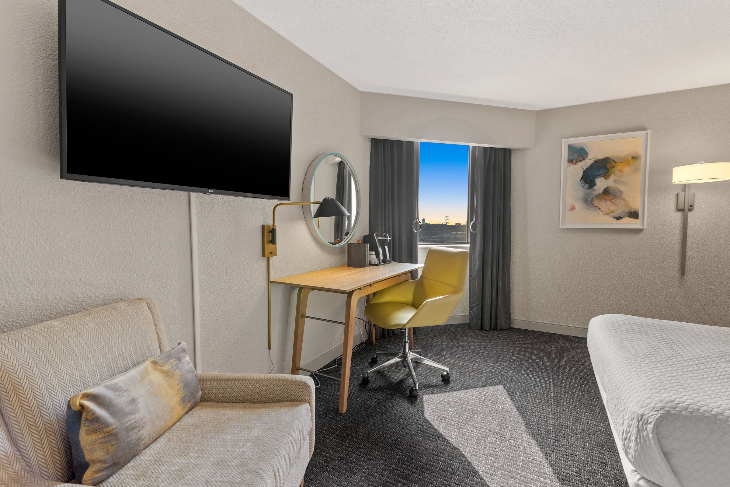 Una camera d'albergo con un letto, una scrivania con una sedia, una televisione, una finestra vista e un quadro appeso al muro.