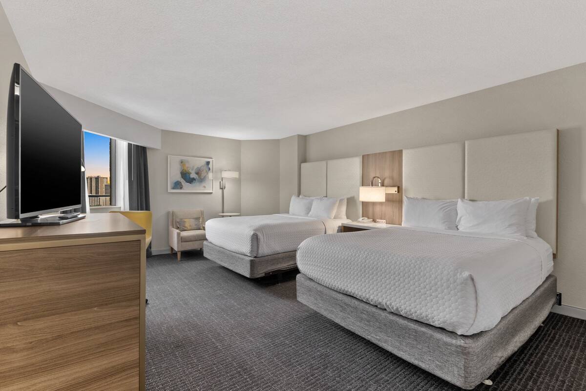 Een hotelkamer met twee bedden, een bureau, een televisie en uitzicht op de stad.