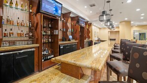 Eine Bar mit einer langen Theke, mehreren Regalen voller Flaschen und einem Fernsehbildschirm.